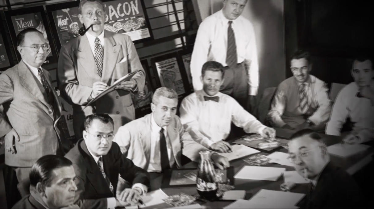 1950s image of white men sitting around conference table